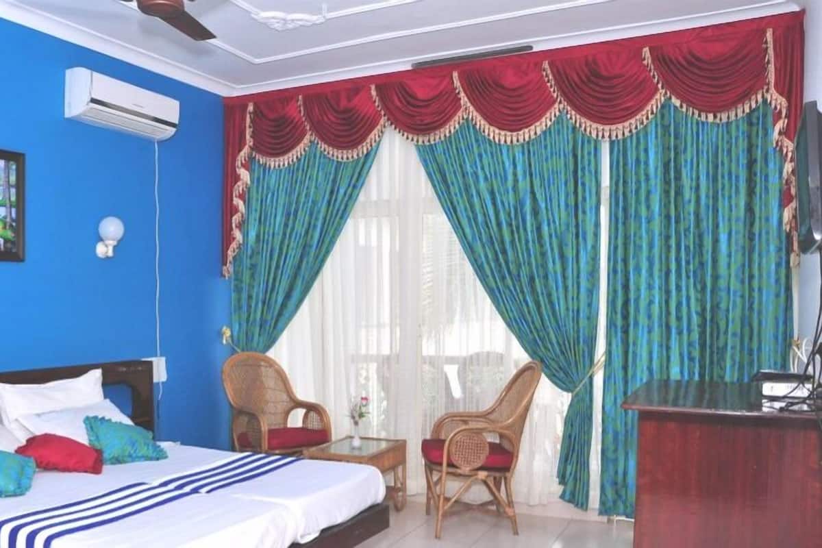 Una habitación de hotel con una cama, dos sillas, un escritorio y un ventanal con cortinas.