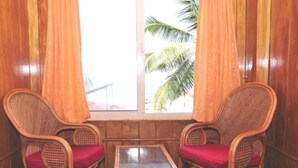 Two wicker chairs with red cushions facing a window with curtains, overlooking palm trees. - Jeevan Ayurvedic Beach Resort (Thiruvananthapuram)