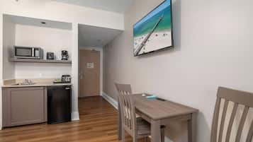 A compact kitchen with a microwave, toaster, and coffee maker, a dining area with a table and chairs, and a beach-themed TV on the wall.