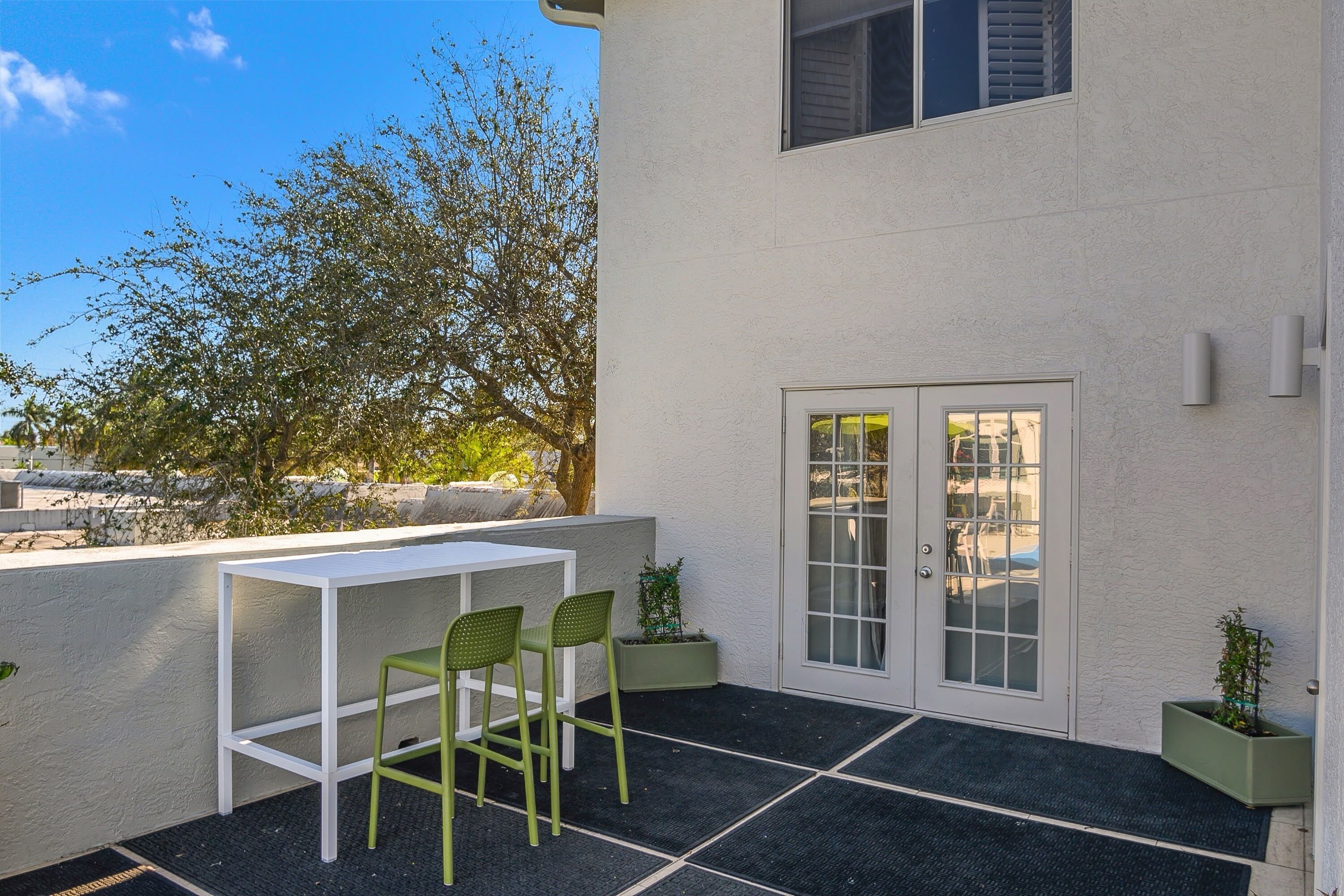 A patio with a white table and two green chairs, a door with glass panels, and a potted plant.