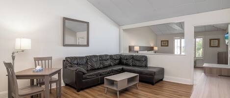 A modern living room with a sectional sofa, a dining table with chairs, a small coffee table, and a large mirror.
