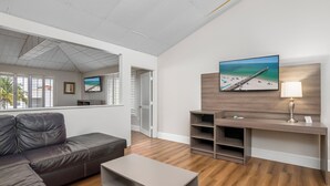 A modern living room with a leather sofa, a coffee table, a TV mounted on a wooden wall, and a beach-themed painting. - Naples Park Central Hotel (Naples)