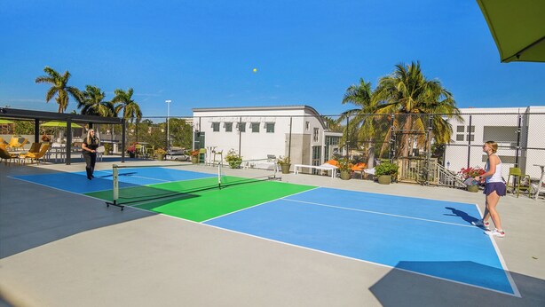 An outdoor tennis court with a net, surrounded by palm trees and a building in the background. - Naples Park Central Hotel (Naples)