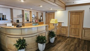 A reception area with a wooden counter, potted plants, a phone, and a sign. - Naples Park Central Hotel (Naples)