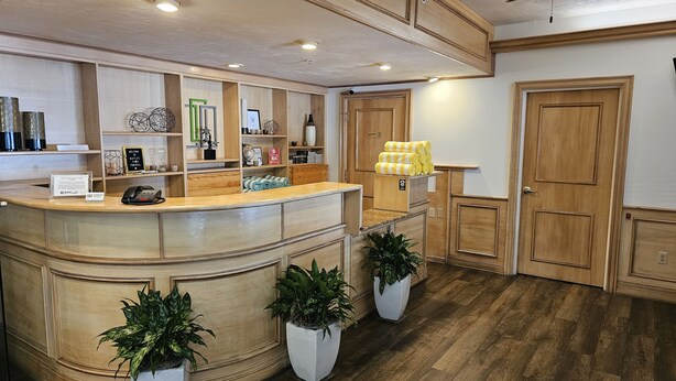 A reception area with a wooden counter, potted plants, a phone, and a sign. - Naples Park Central Hotel (Naples)