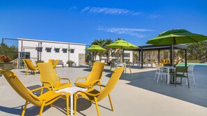 An outdoor patio area with yellow chairs and green umbrellas, a glass-enclosed seating area, and a white building in the background. - Naples Park Central Hotel (Naples)