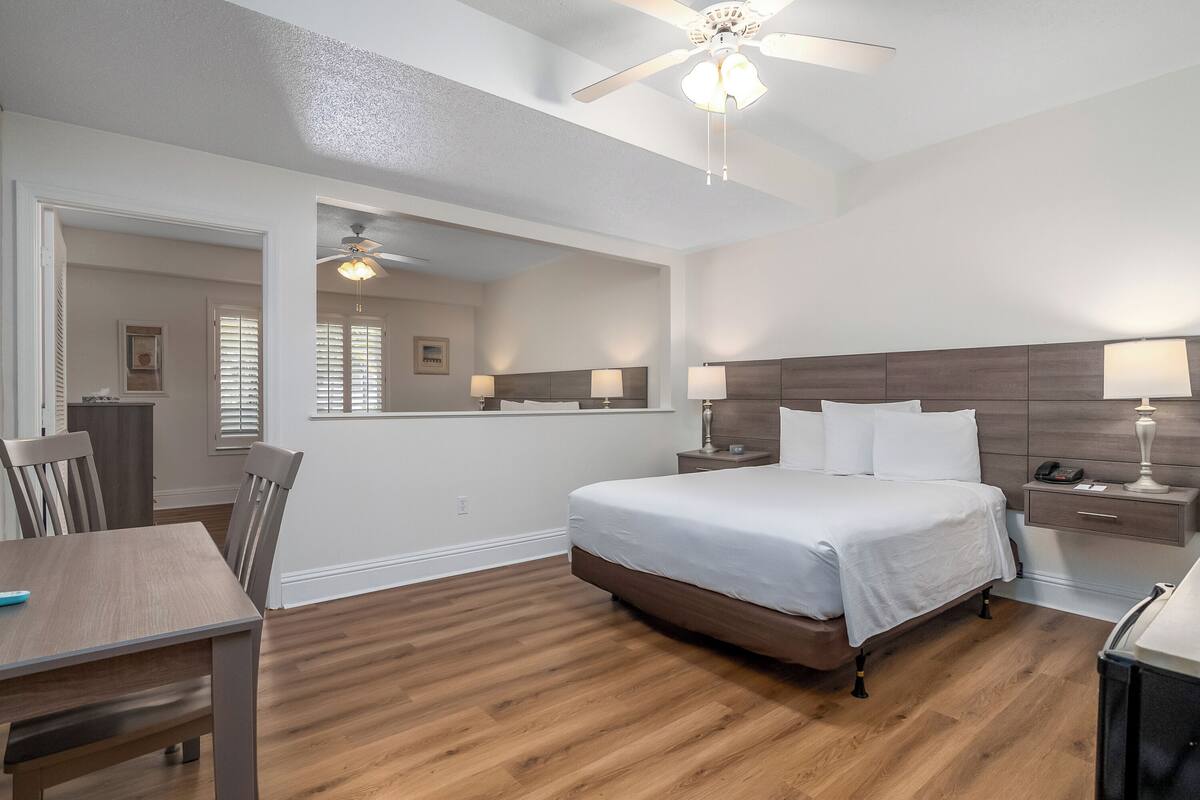 A hotel room with a large bed, a desk, a chair, a nightstand, and a ceiling fan.