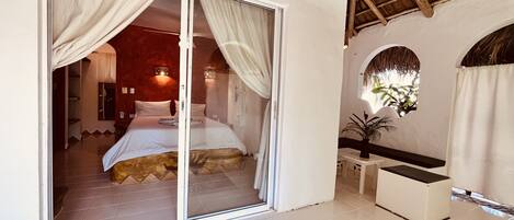 A bedroom with a sliding glass door, a bed with white linens, a small table, and a plant.