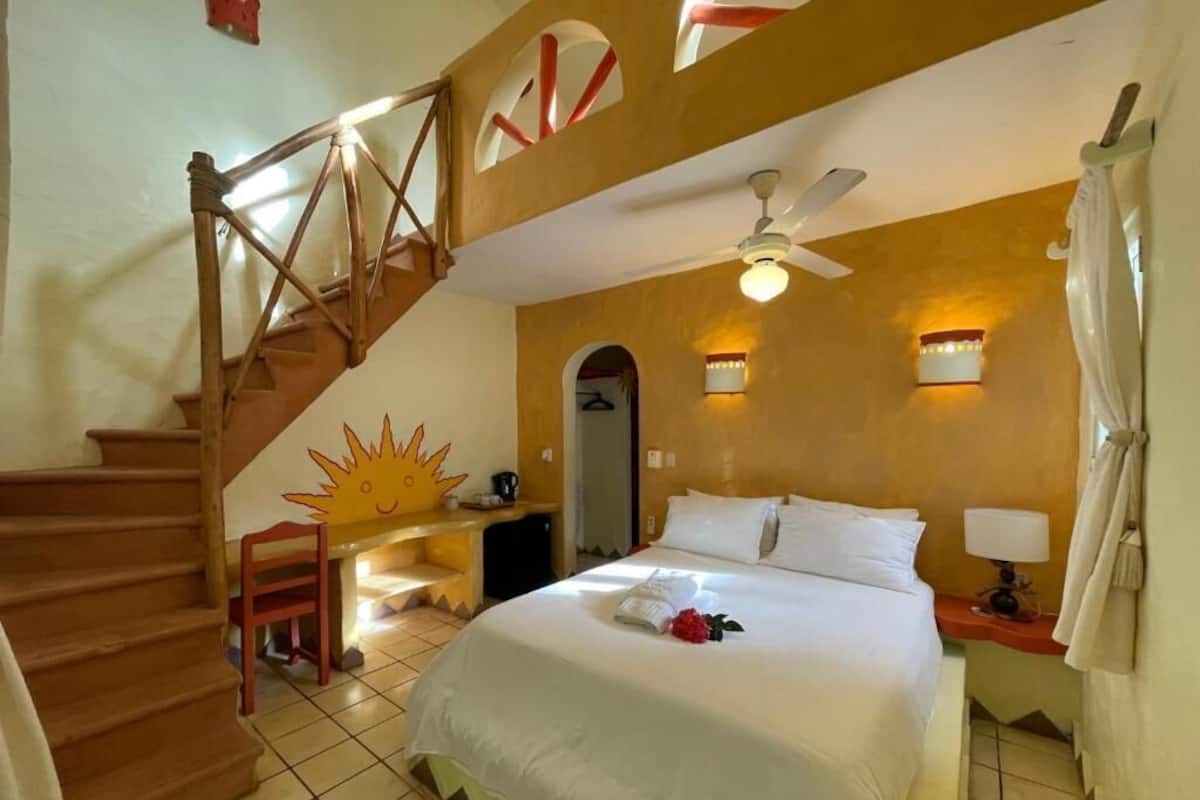 A hotel room with a bed, a desk, a chair, a staircase, and a ceiling fan.