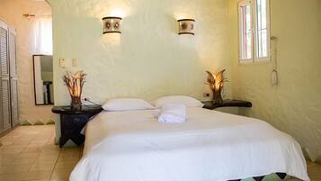 A bedroom with a large bed, two bedside tables with lamps, a window, and a door leading to another room.