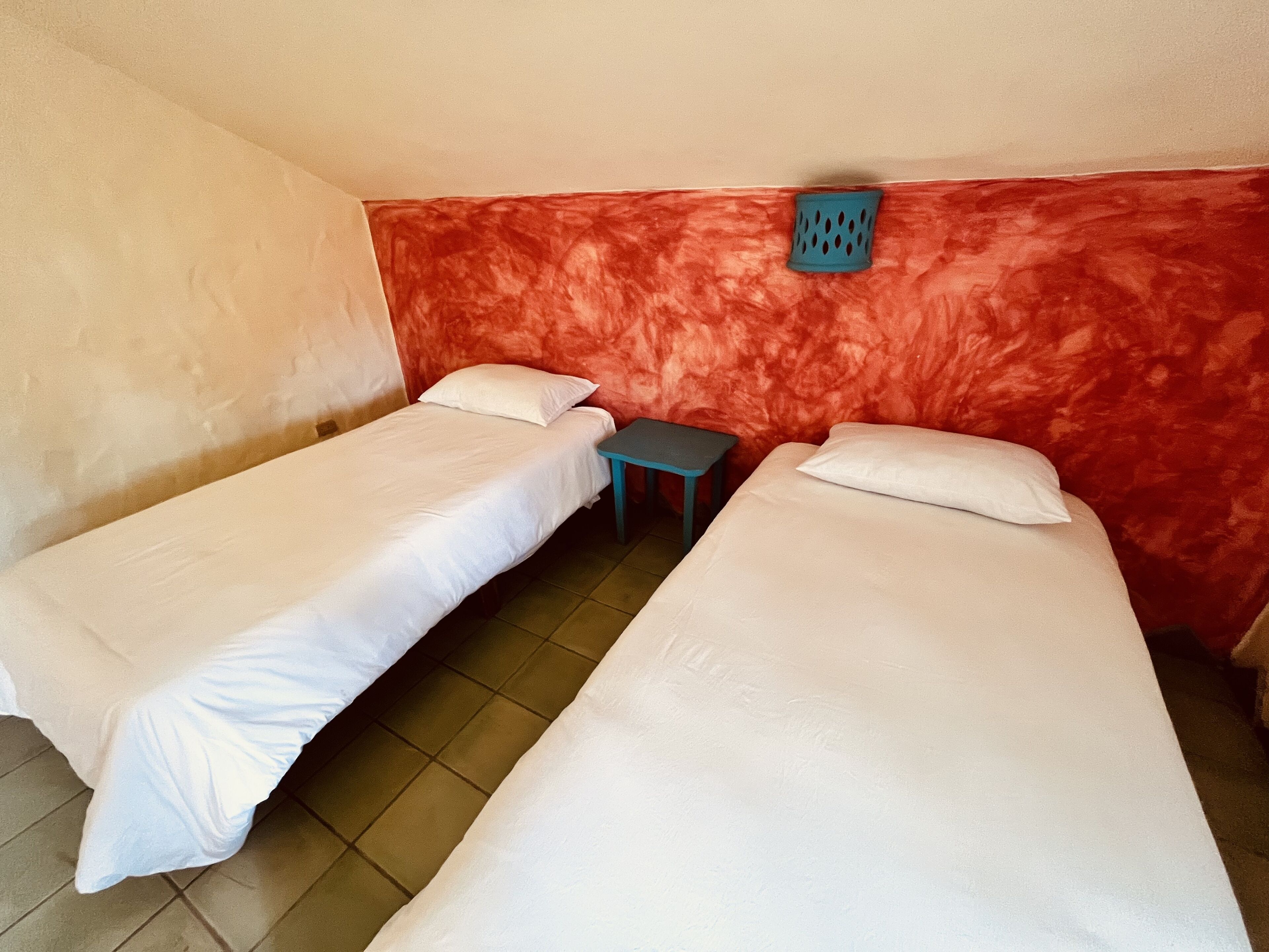 Ein Zimmer mit zwei Einzelbetten, einem kleinen Tisch und einer roten Wand mit Struktur.