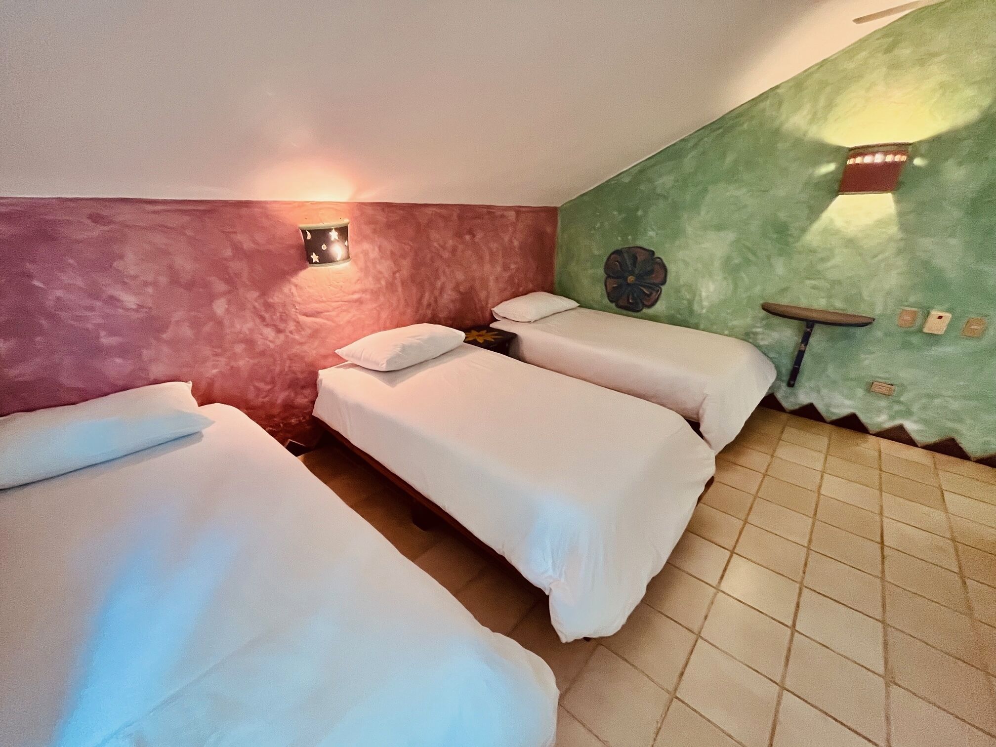 A room with three single beds, a small table, and a wall-mounted light fixture.