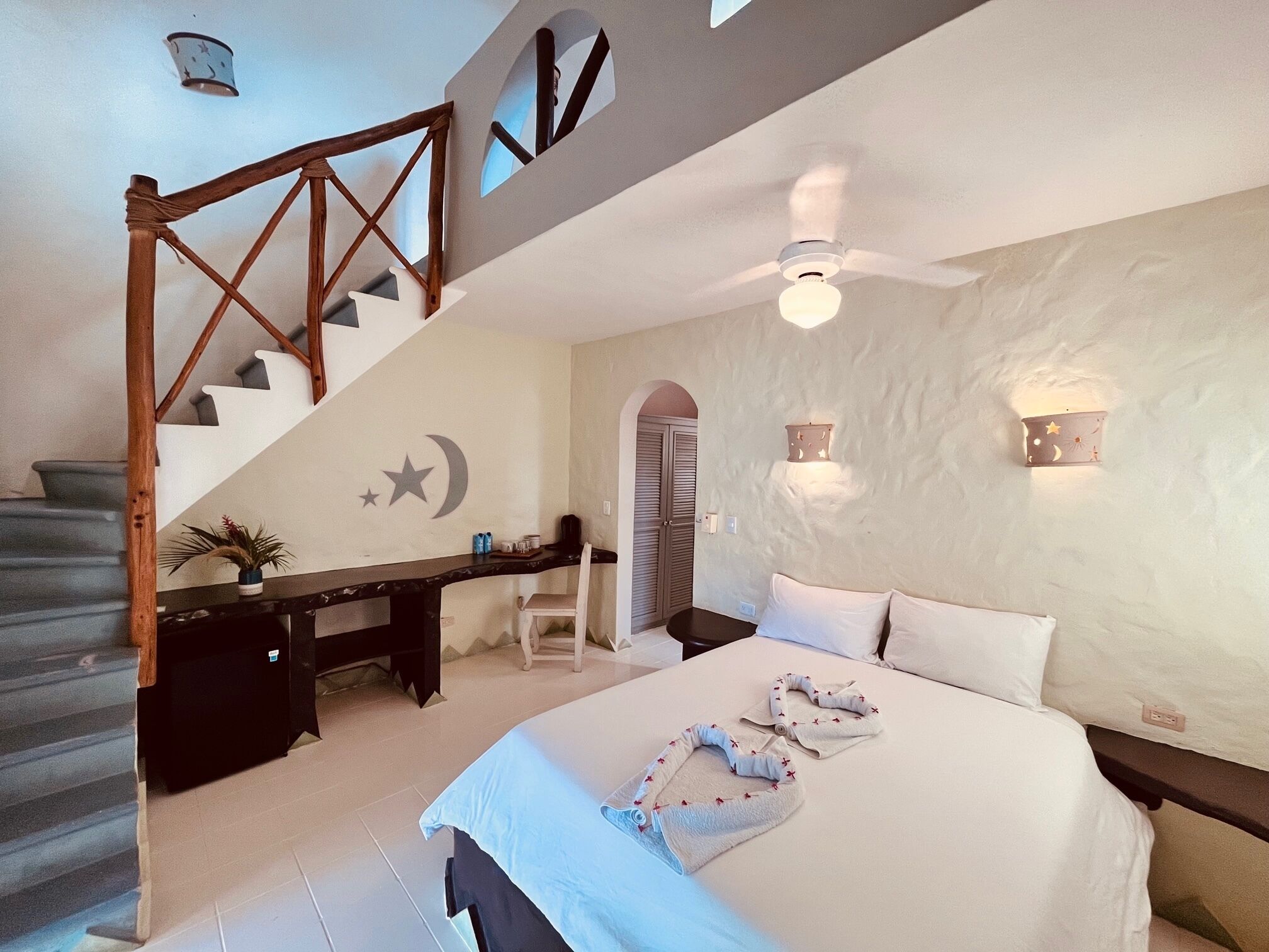 Une chambre avec un grand lit, un escalier en bois, un bureau et une chaise.
