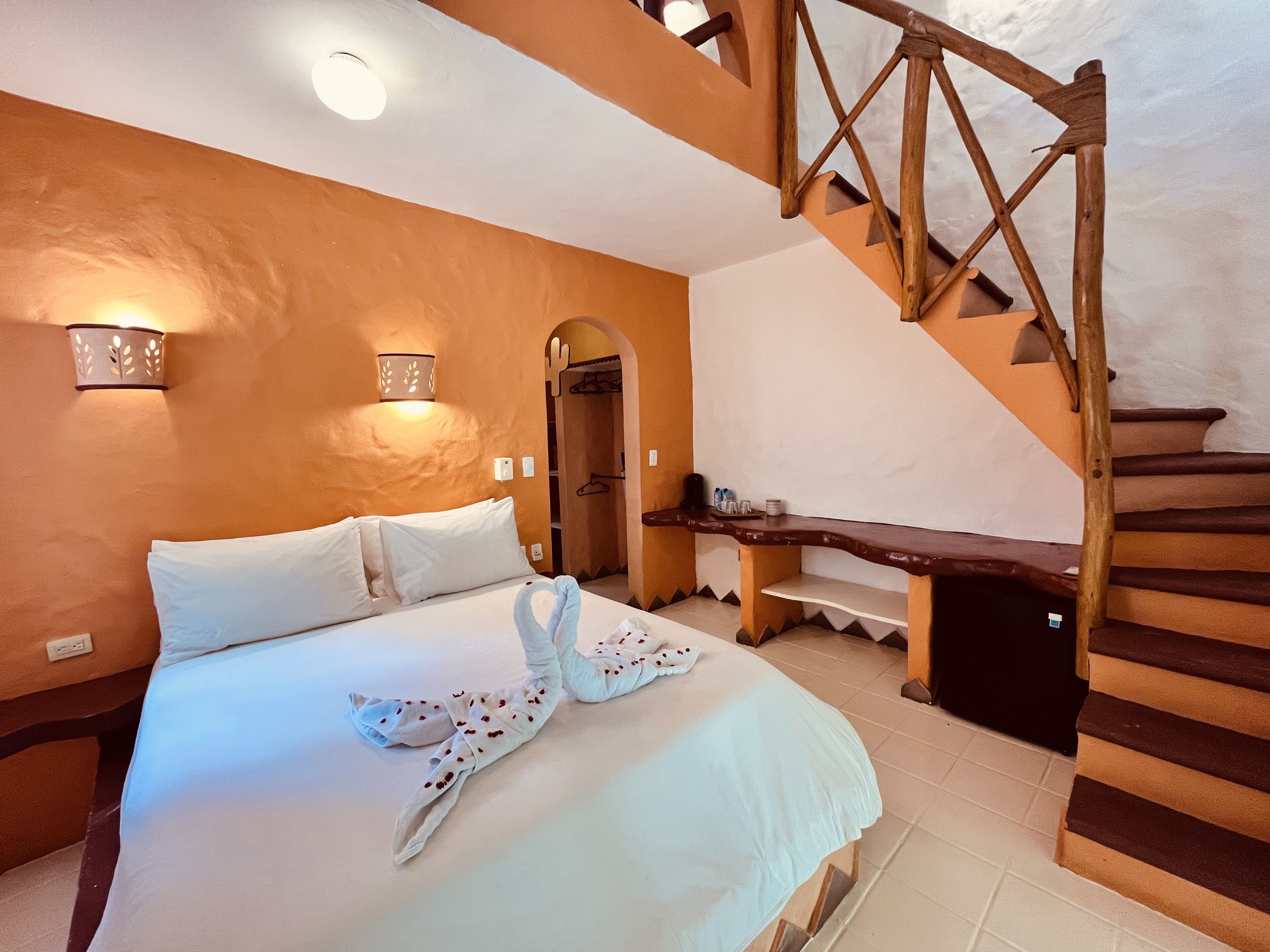 Un dormitorio con una cama, una escalera de madera y una lámpara fijada a la pared.