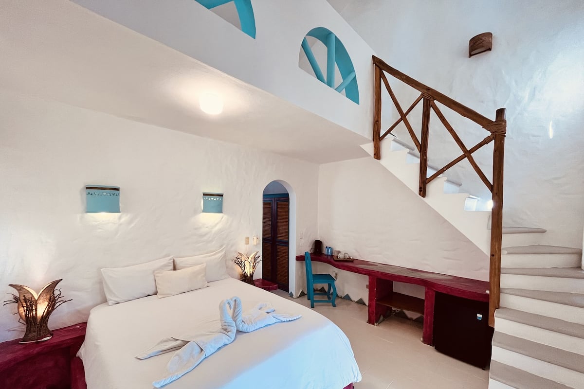 A bedroom with a bed, a desk, and a staircase.