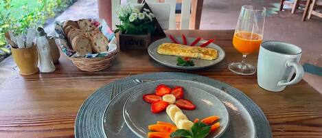 Un desayuno con una fuente de fruta, un vaso de zumo de naranja y una taza sobre una mesa de madera.
