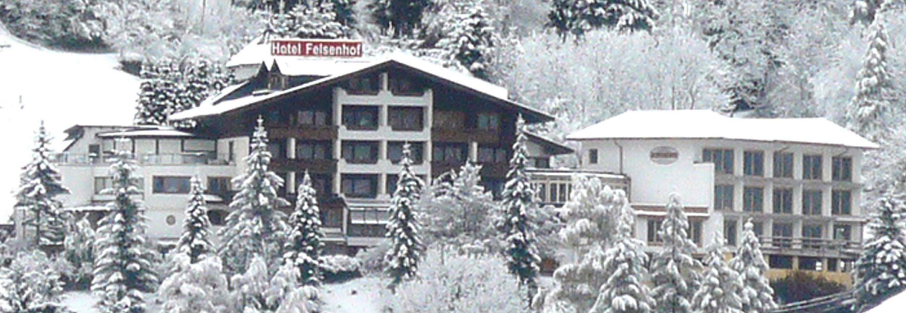 Egy „Hotel Felsenhof” feliratú táblával ellátott szálloda, melyet hóval borított fák vesznek körül.