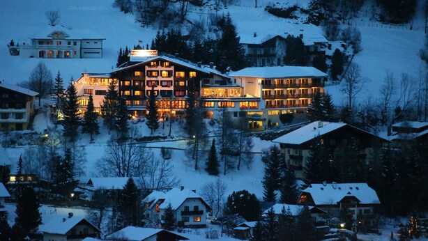 Un hotel grande de varios pisos con un letrero llamativo, rodeado de árboles y edificios cubiertos de nieve.