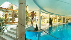 Una piscina interior con techo de cristal, escalones de mármol y tumbonas.