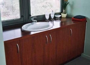A kitchen with a white sink, wooden cabinets, and a window with blinds. - Red Brier Cottage Accommodation (Richmond)