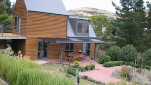 A modern wooden house with a sloped roof, a covered patio, and a landscaped garden. - Red Brier Cottage Accommodation (Richmond)