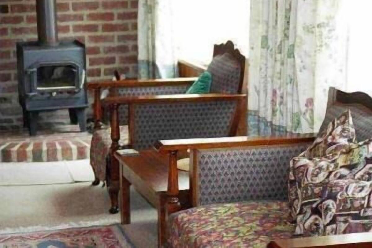 A cozy living room with a brick fireplace, wooden furniture, and patterned upholstery.