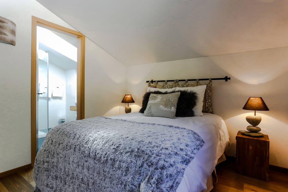 Une chambre à coucher avec un grand lit, deux lampes de chevet, une tête de lit agrémentée de coussins décoratifs et une table de chevet en bois.