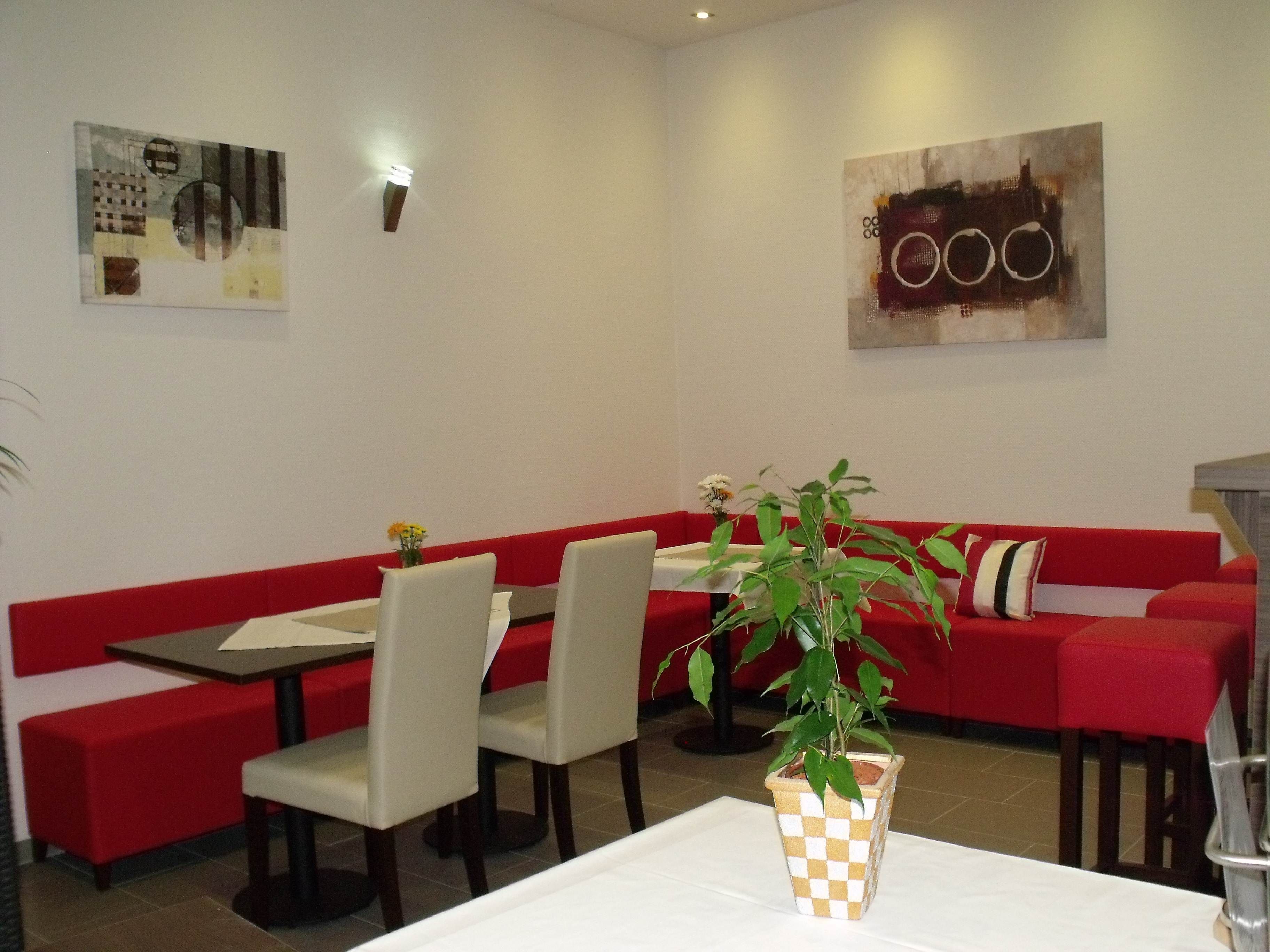 A restaurant with red seating, white tables, and a potted plant on a table.