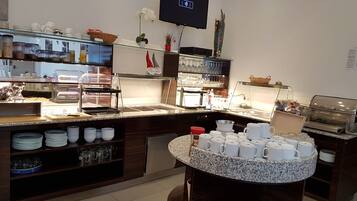 Zona de bufé con diversas opciones de comida y bebida, incluyendo una estación de café y una exhibición de platos y tazones.