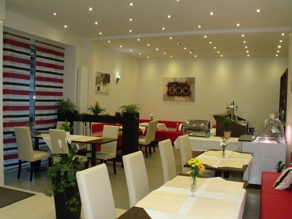 Un restaurant avec des tables dressées pour le service, des chaises et un espace buffet.