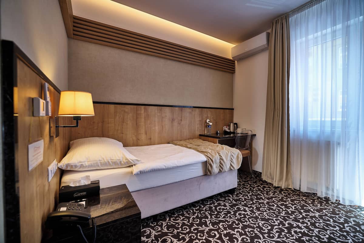 A hotel room with a bed, bedside lamp, phone, and a desk with a lamp.