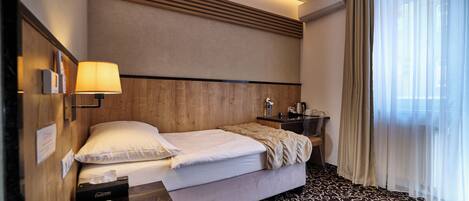 A hotel room with a bed, bedside lamp, phone, and a desk with a lamp.