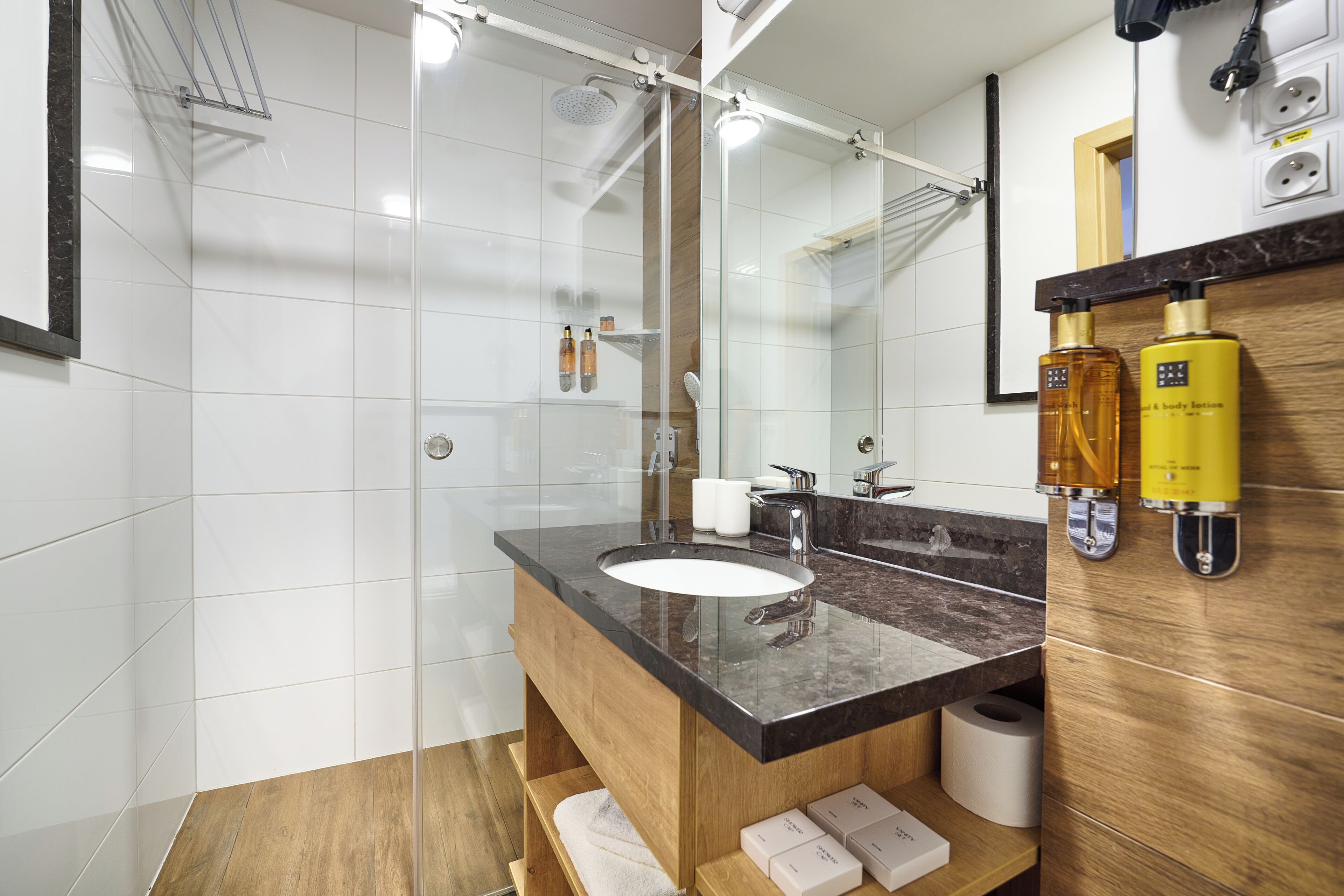 Un baño moderno con cabina de ducha de vidrio, tocador de madera con encimera de mármol y un espejo grande.