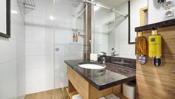 Un baño moderno con cabina de ducha de vidrio, tocador de madera con encimera de mármol y un espejo grande.