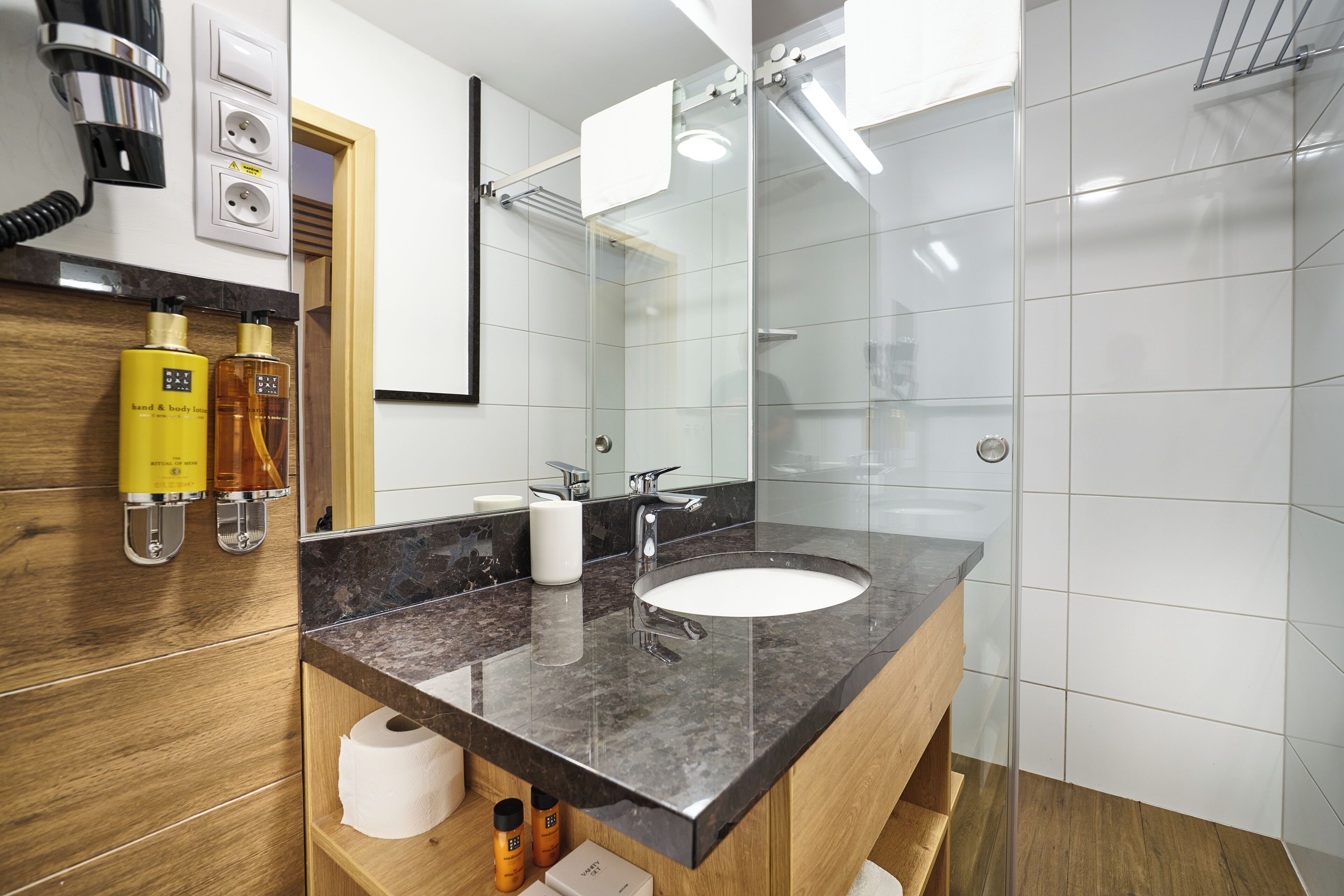Ein modernes Badezimmer mit Marmorwaschbecken, einer Duschkabine aus Glas und einem Holzbadezimmerkorpus.