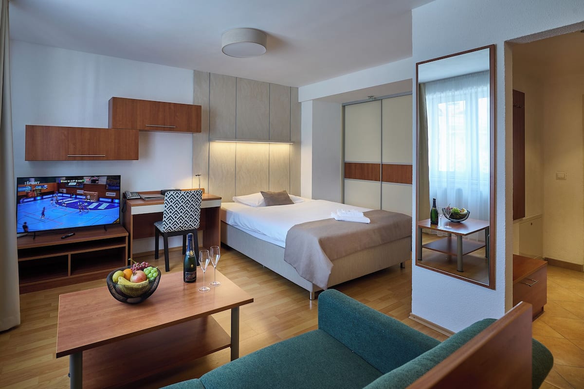 A hotel room with a bed, a TV, a desk with a chair, a sofa, and a mirror.