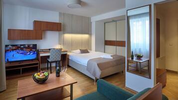 A hotel room with a bed, a TV, a desk with a chair, a sofa, and a mirror.