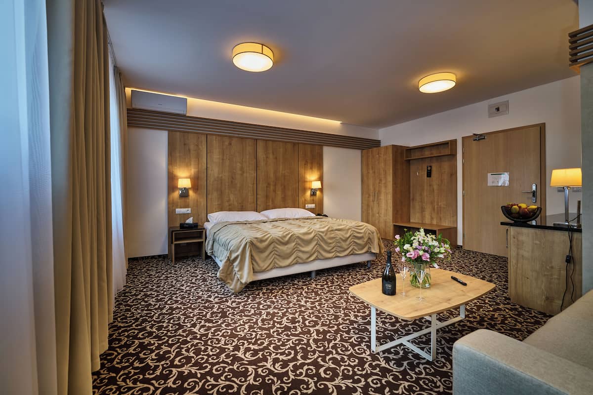 A hotel room with a bed, bedside lamps, a wooden headboard, a small table with a vase of flowers, and a desk with a bowl of fruit.