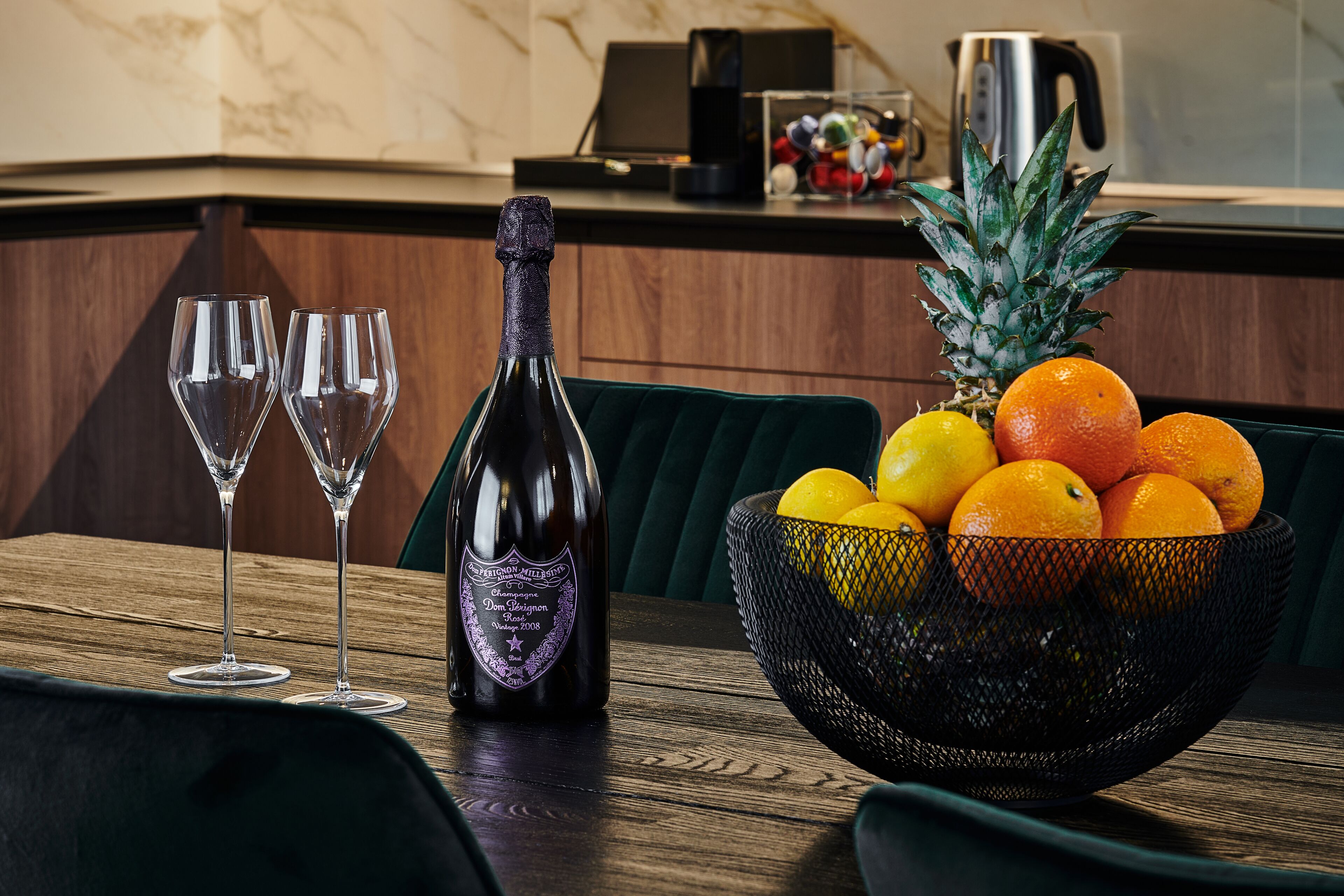 Una mesa de comedor con una botella de champán, dos copas y un cuenco de fruta.