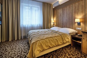 Una habitación de hotel con cama, cortinas, una lámpara de pared y alfombra estampada.