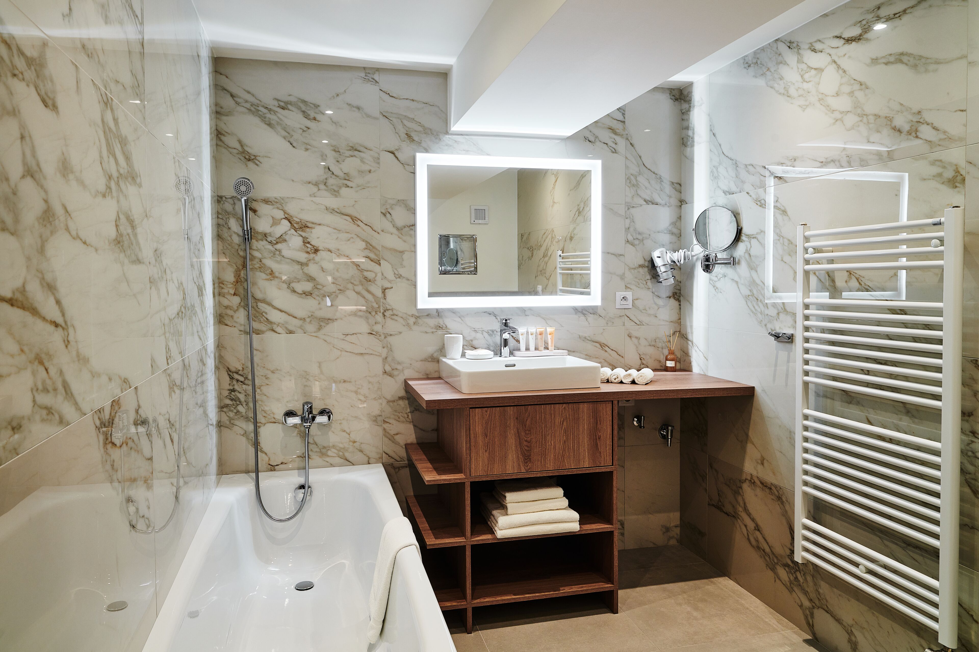A modern bathroom with a marble wall, a bathtub, a vanity with a mirror, and a towel rack.