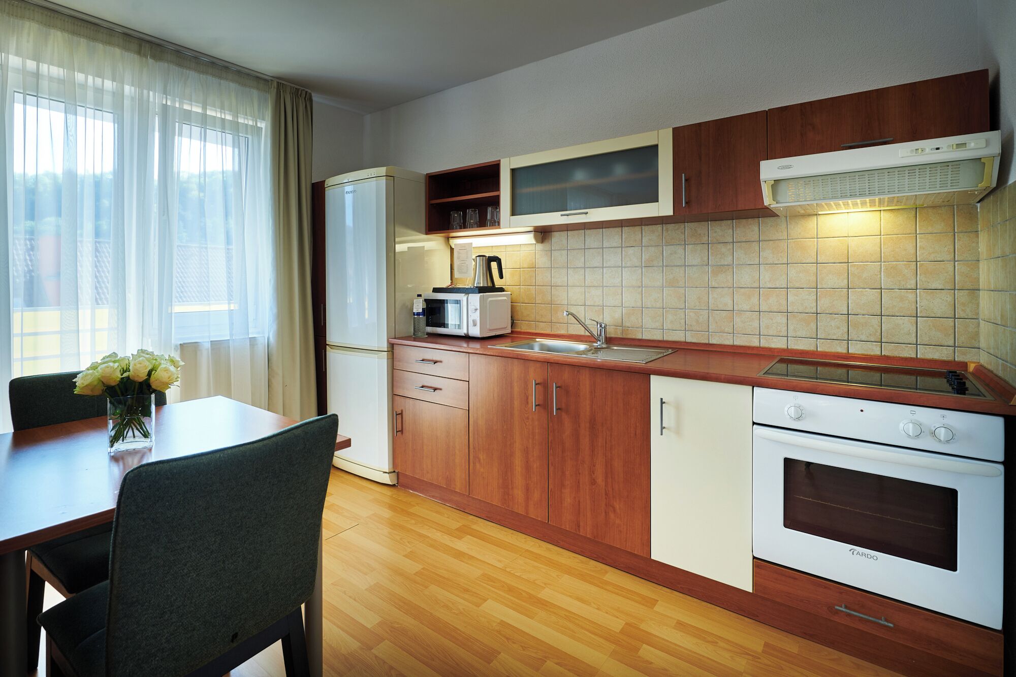Cocina compacta con armarios de madera, microondas integrado, estufa y pileta.