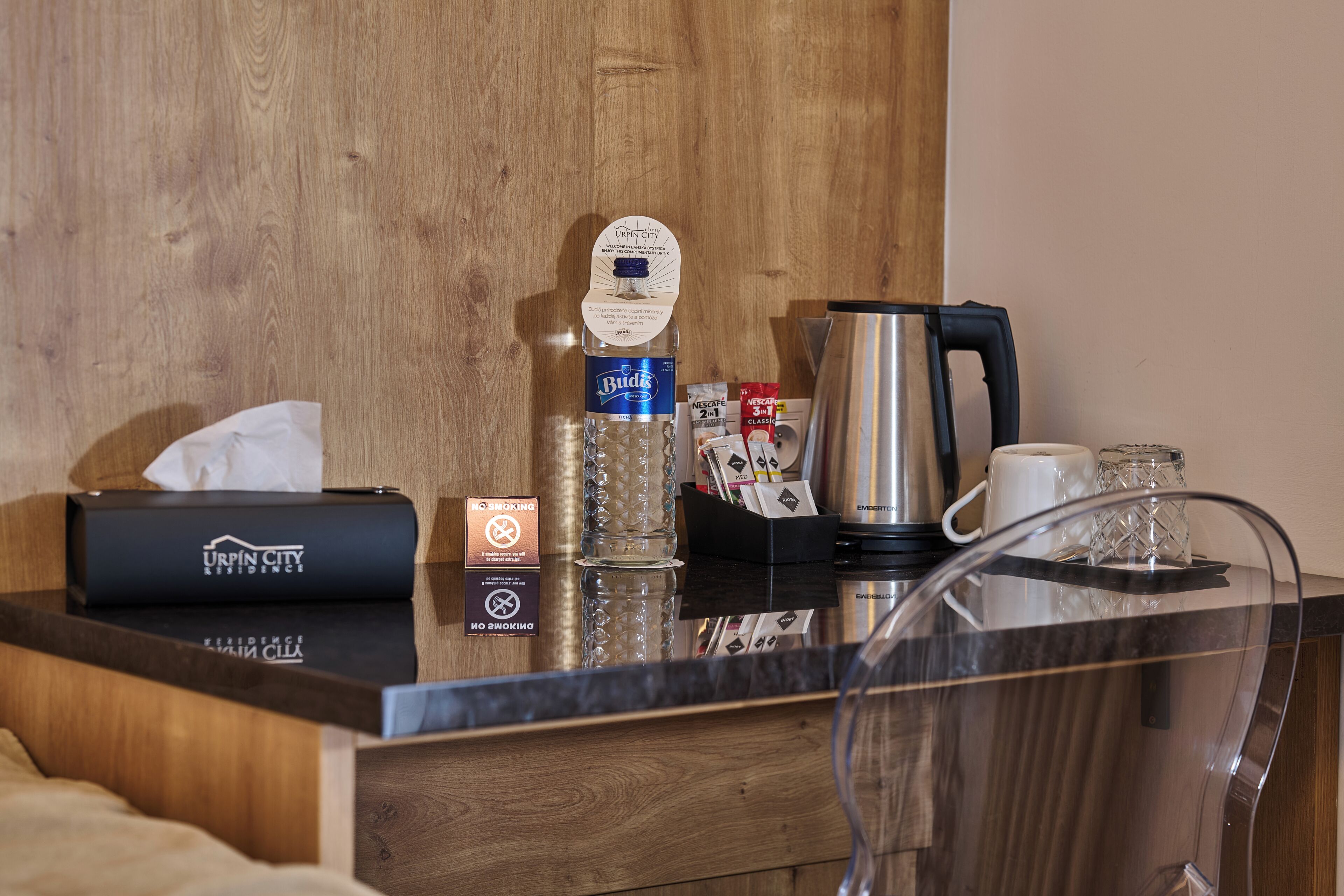 Zona de recepción de un hotel con una pared de madera, una botella de Budweiser, una cafetera, una caja de pañuelos y una jarra de vidrio.