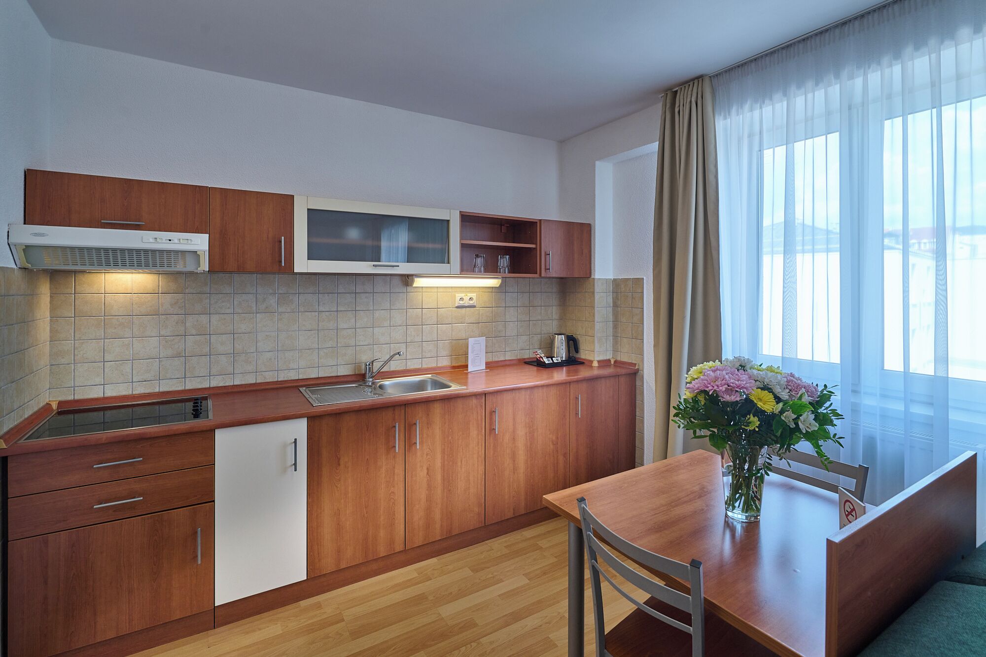 Una cocina moderna con armarios de madera, un lavamanos de acero inoxidable y una zona de comedor con mesa y sillas.