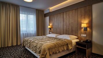 Habitación de hotel con cama, cortinas, cabecero de madera, dos lámparas fijadas a la pared y una mesita de noche con un teléfono.