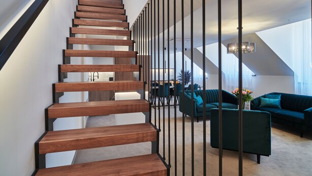 Una escalera moderna con escalones de madera y barandillas negras que conduce a una sala de estar con sofás color turquesa y una mesa de centro.