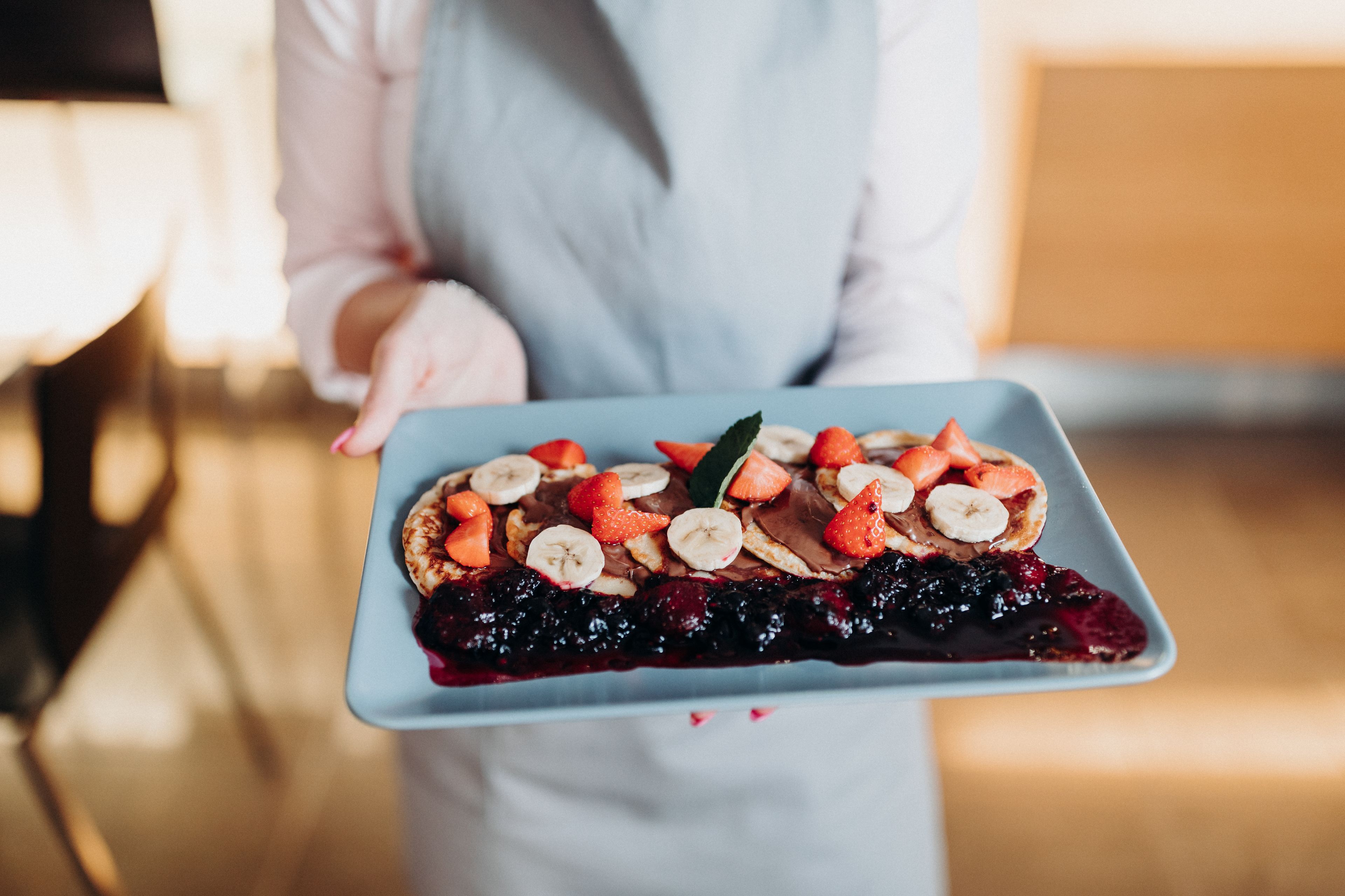 A person holding a rectangular plate with a dessert topped with strawberries, bananas, and chocolate.