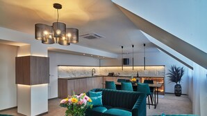Una sala de estar moderna con un sofá verde, una mesa de centro con flores y una cocina al fondo.
