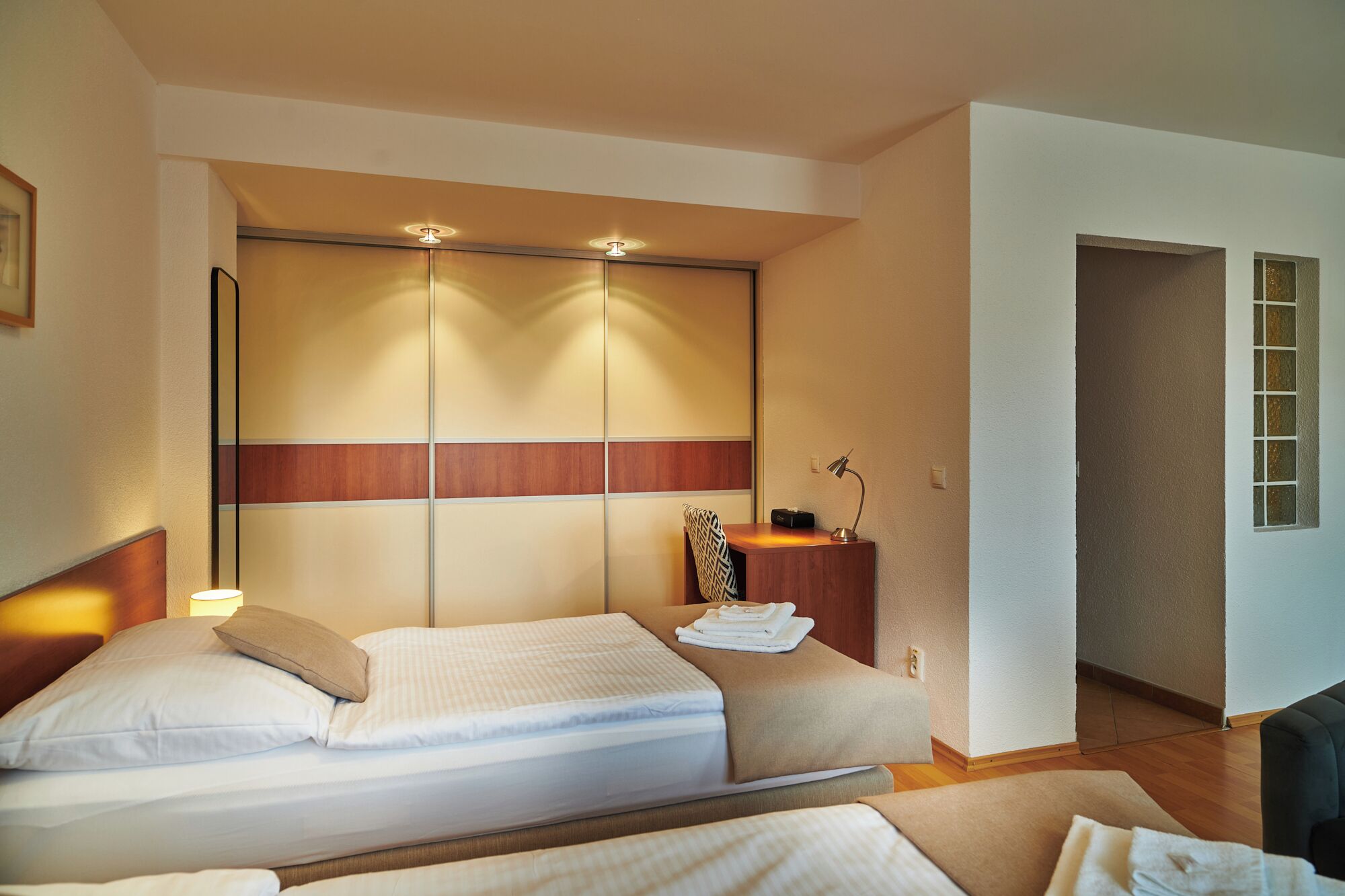 A hotel room with a bed, bedside table, lamp, and a view of the hallway.