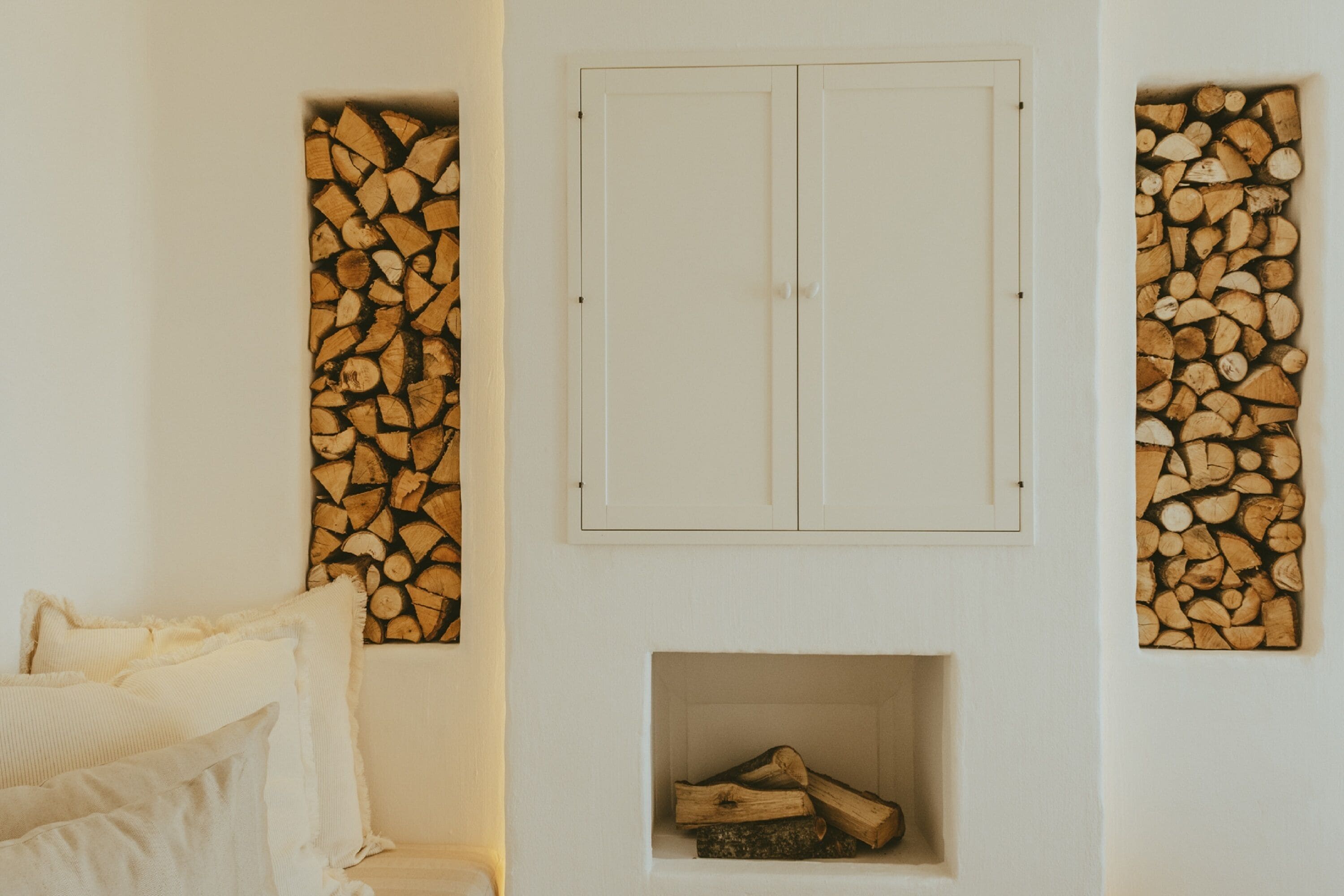 Ein Zimmer mit einem weißen Wandschrank, einem Kamin mit Holzscheiten und einem Bett mit weißer Bettwäsche.